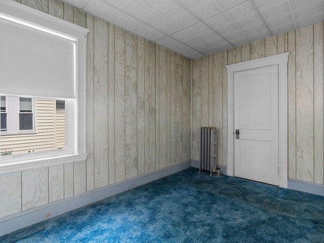 carpeted spare room featuring radiator, baseboards, and wooden walls