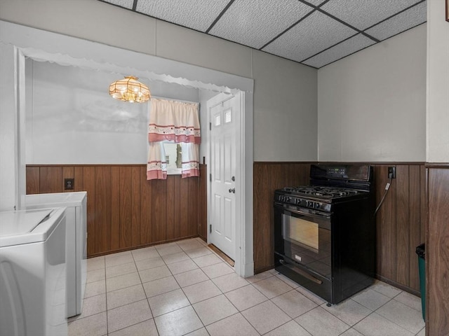 kitchen with black gas stove, a wainscoted wall, wooden walls, washer and dryer, and light tile patterned floors