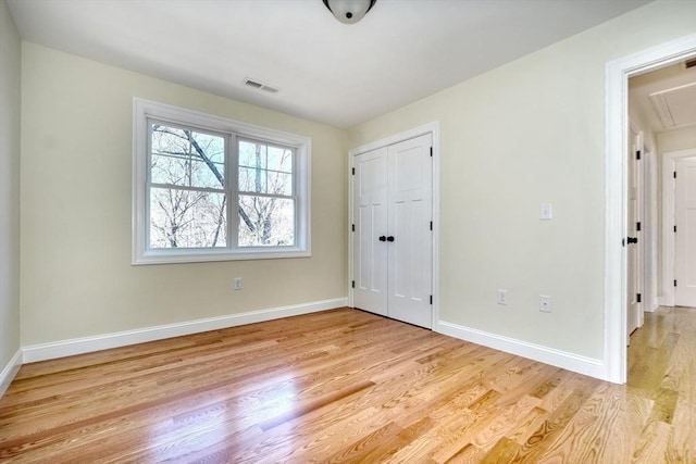 unfurnished bedroom featuring a closet, attic access, light wood-type flooring, baseboards, and visible vents