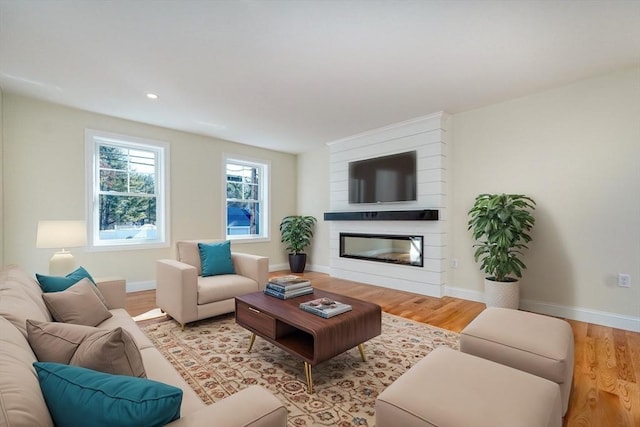 living area with baseboards, wood finished floors, a large fireplace, and recessed lighting