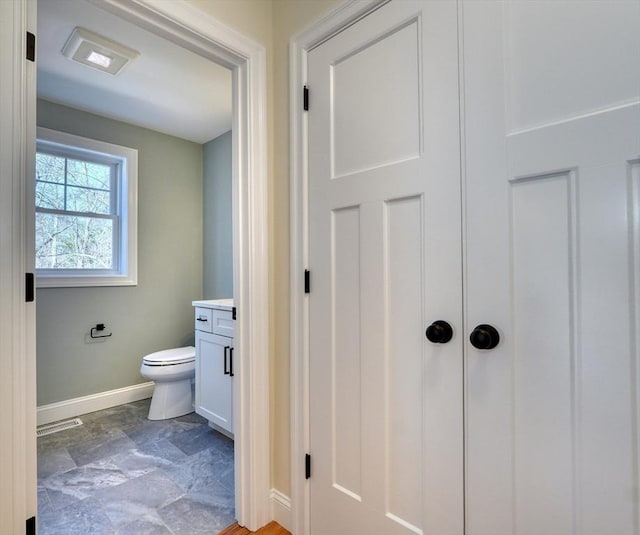 bathroom with toilet, vanity, baseboards, stone finish floor, and visible vents