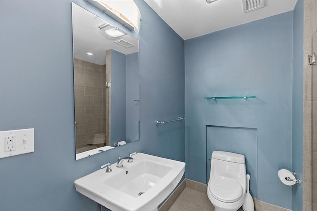 bathroom featuring sink, tile patterned flooring, a tile shower, and toilet