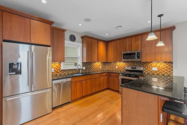 kitchen featuring appliances with stainless steel finishes, hanging light fixtures, light hardwood / wood-style floors, a breakfast bar, and sink