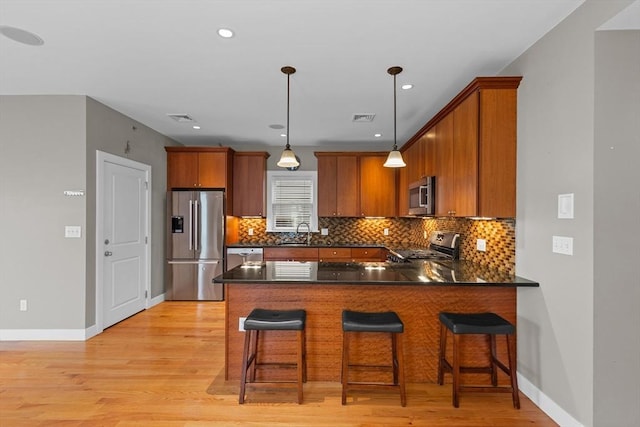 kitchen with decorative light fixtures, light hardwood / wood-style floors, appliances with stainless steel finishes, a kitchen breakfast bar, and sink