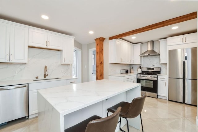 kitchen with appliances with stainless steel finishes, sink, white cabinetry, and wall chimney range hood