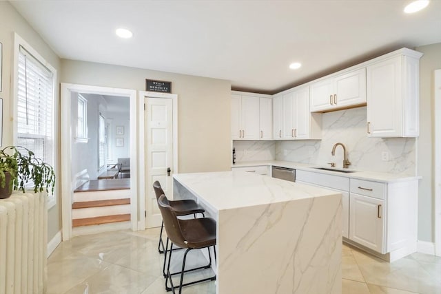 kitchen featuring light stone countertops, white cabinets, radiator heating unit, a center island, and sink