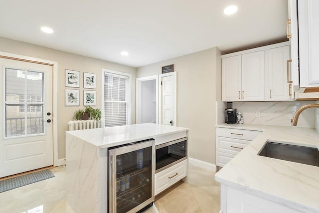 kitchen with wine cooler, sink, light stone countertops, built in microwave, and white cabinets