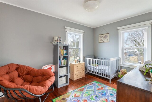 bedroom with dark hardwood / wood-style flooring, crown molding, multiple windows, and a crib