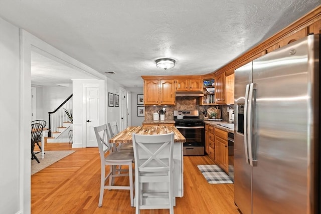 45 S Elm St, West Bridgewater, MA 02379 - kitchen with appliances with stainless steel finishes, under cabinet range hood, light wood-style flooring, tasteful backsplash, and brown cabinetry