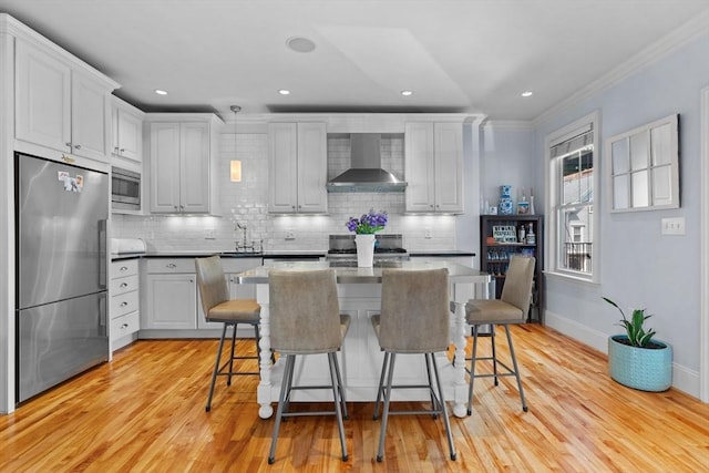 kitchen featuring stainless steel appliances, tasteful backsplash, wall chimney range hood, crown molding, and light wood-style flooring