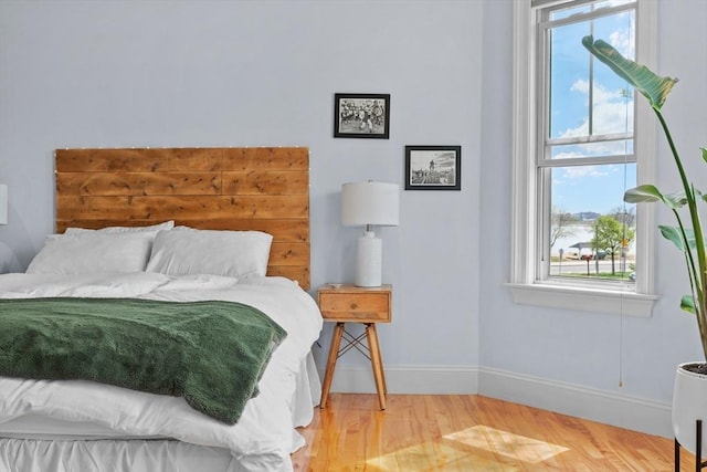 bedroom with multiple windows, wood finished floors, and baseboards