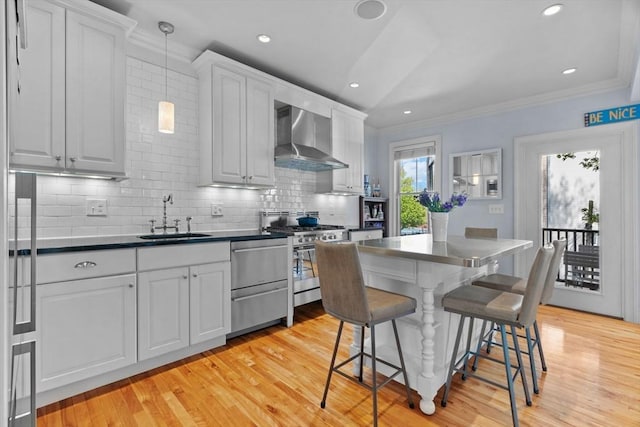 kitchen with ornamental molding, a sink, wall chimney range hood, dark countertops, and appliances with stainless steel finishes