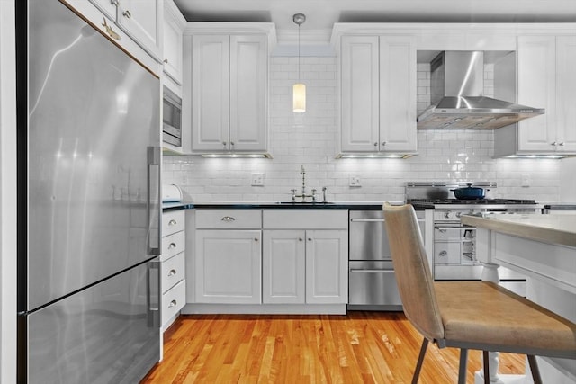 kitchen featuring white cabinetry, appliances with stainless steel finishes, a sink, and wall chimney exhaust hood