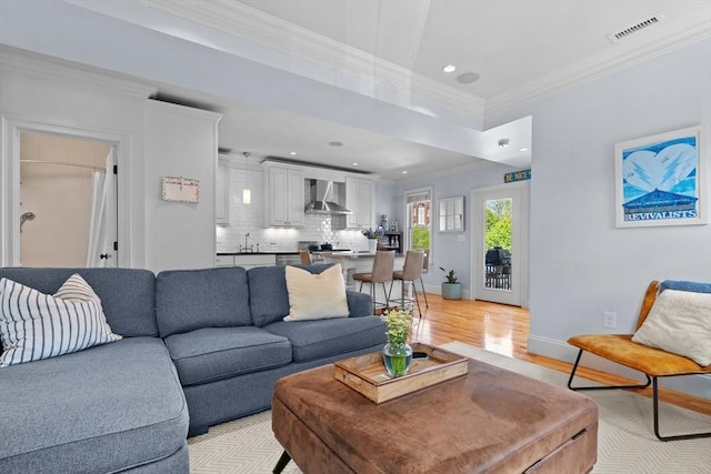 living room featuring crown molding, light wood-type flooring, visible vents, baseboards, and recessed lighting