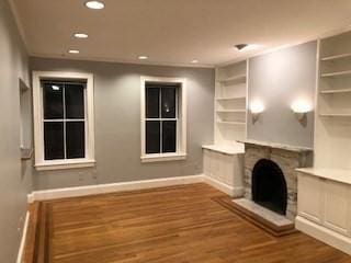 unfurnished living room with recessed lighting, a fireplace with raised hearth, baseboards, and wood finished floors