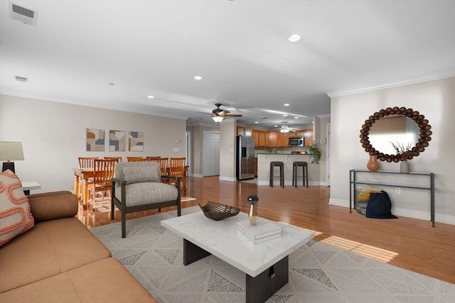 living room featuring crown molding, ceiling fan, and light wood-type flooring