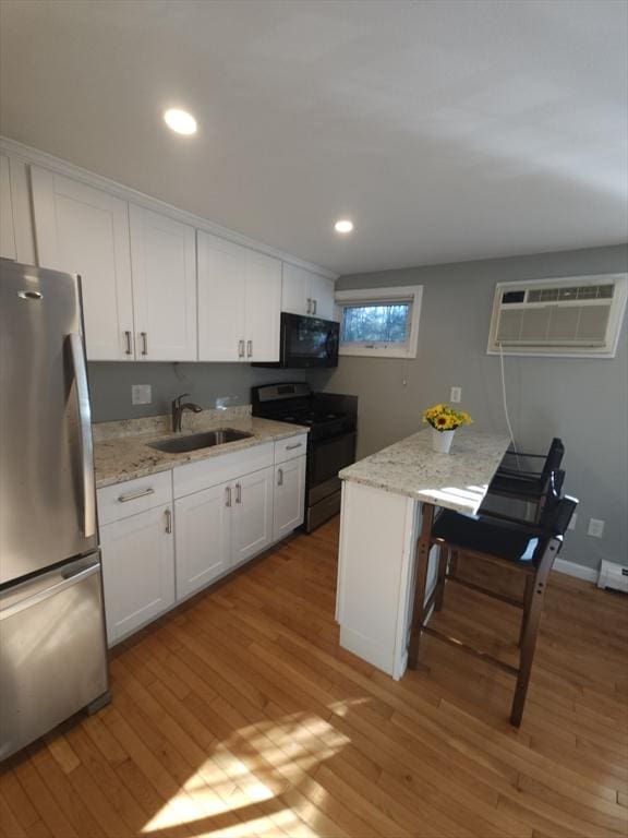 kitchen with sink, appliances with stainless steel finishes, a wall mounted AC, light hardwood / wood-style floors, and white cabinets