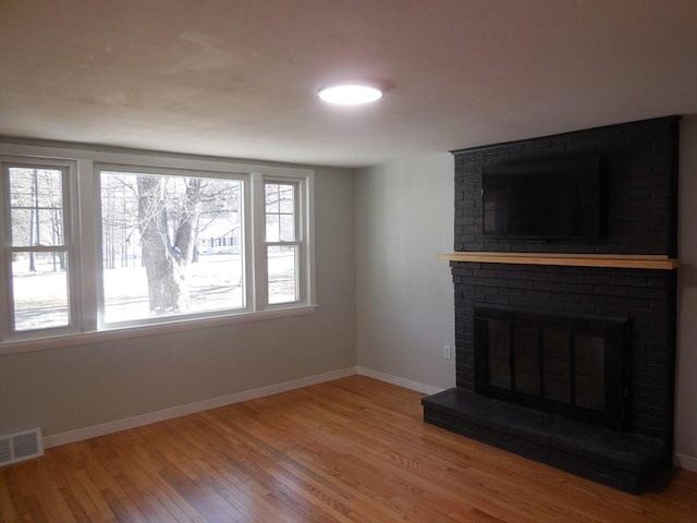 unfurnished living room featuring a brick fireplace, a wealth of natural light, and wood-type flooring