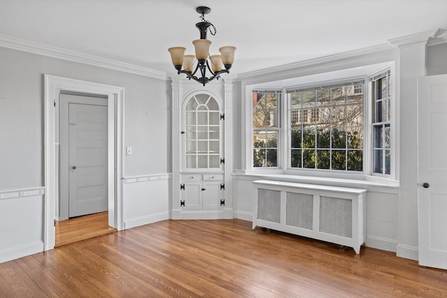 unfurnished dining area with crown molding, radiator heating unit, a chandelier, and hardwood / wood-style flooring