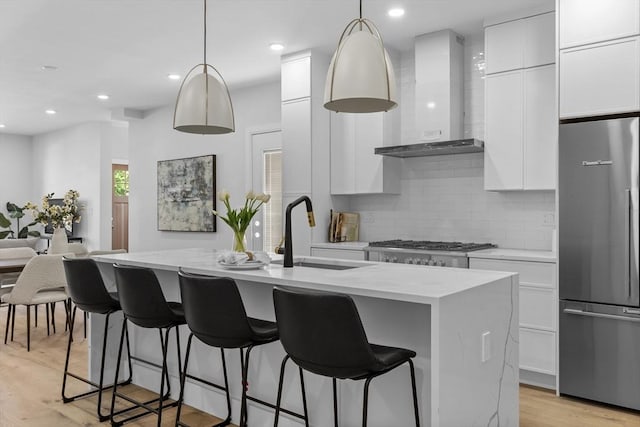 kitchen featuring built in refrigerator, wall chimney exhaust hood, decorative light fixtures, sink, and a center island with sink