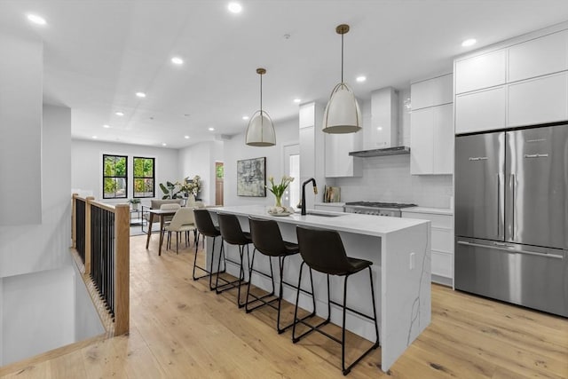 kitchen with a kitchen island with sink, wall chimney range hood, stainless steel appliances, and white cabinetry