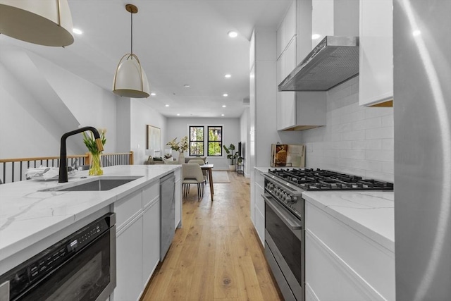 kitchen with decorative light fixtures, wall chimney range hood, sink, white cabinetry, and appliances with stainless steel finishes