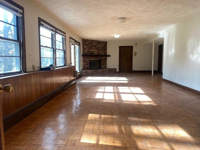 unfurnished living room with a baseboard heating unit, a brick fireplace, wood walls, a textured ceiling, and baseboards