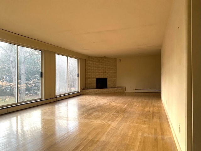 unfurnished living room featuring a brick fireplace, plenty of natural light, baseboard heating, and light wood-style flooring