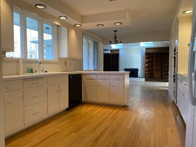 kitchen featuring light wood finished floors, light countertops, white cabinetry, a sink, and a peninsula