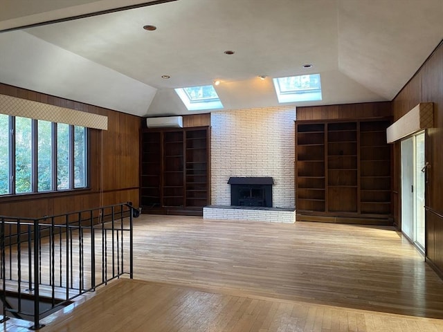 unfurnished living room featuring vaulted ceiling with skylight, light wood-type flooring, built in features, and wooden walls