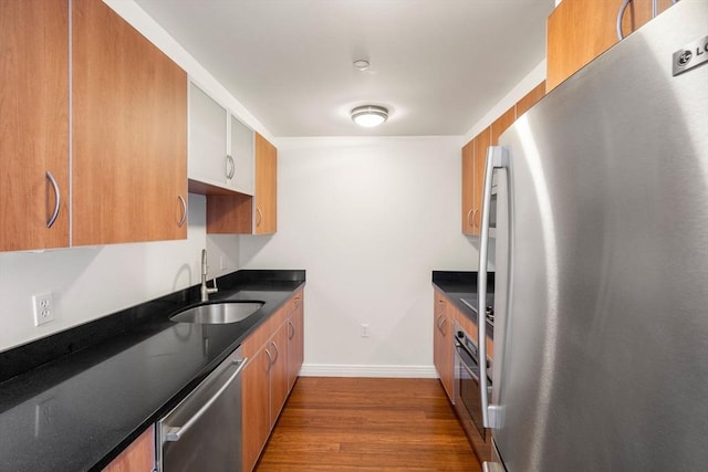 kitchen featuring stainless steel appliances, a sink, dark wood-type flooring, baseboards, and brown cabinets
