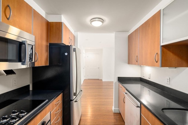 kitchen featuring stainless steel microwave, black electric cooktop, dishwashing machine, brown cabinetry, and wood finished floors