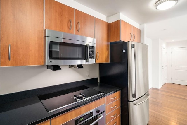 kitchen with appliances with stainless steel finishes, brown cabinets, dark countertops, and light wood finished floors