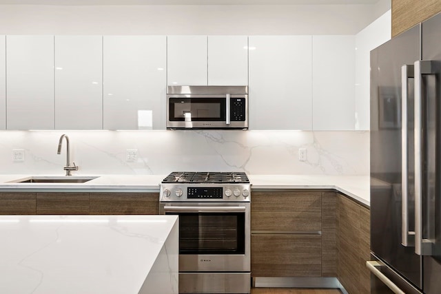 kitchen featuring tasteful backsplash, light stone counters, premium appliances, sink, and white cabinets