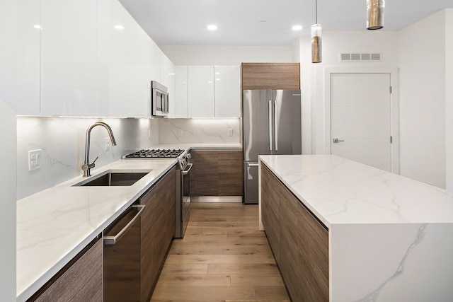 kitchen featuring sink, stainless steel appliances, light hardwood / wood-style flooring, pendant lighting, and white cabinets