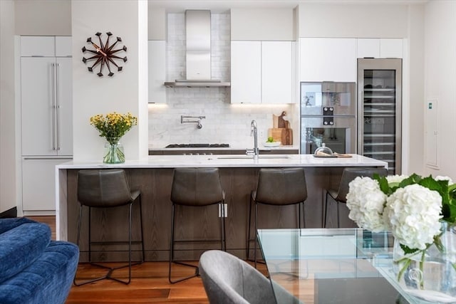 kitchen featuring decorative backsplash, hardwood / wood-style floors, white cabinetry, kitchen peninsula, and wall chimney exhaust hood