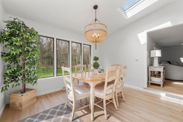 dining space with baseboards, light wood-style flooring, a notable chandelier, and a skylight