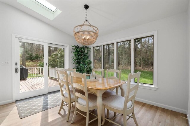 dining space with vaulted ceiling with skylight, baseboards, light wood finished floors, and a chandelier