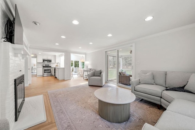 living room with a fireplace, recessed lighting, ornamental molding, and light wood-type flooring