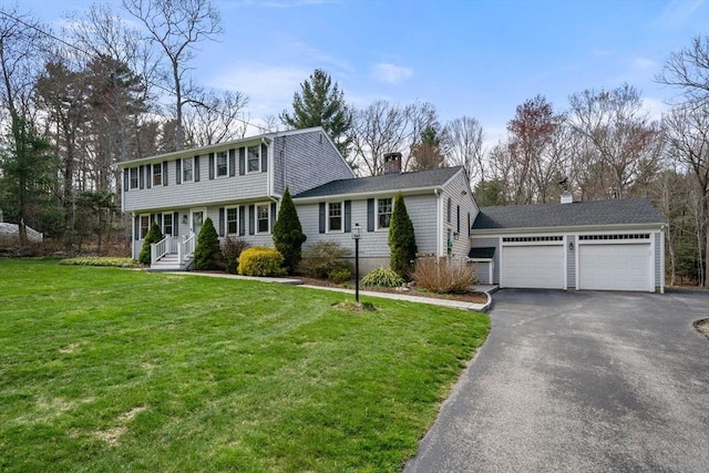 colonial-style house featuring an attached garage, driveway, a chimney, and a front yard