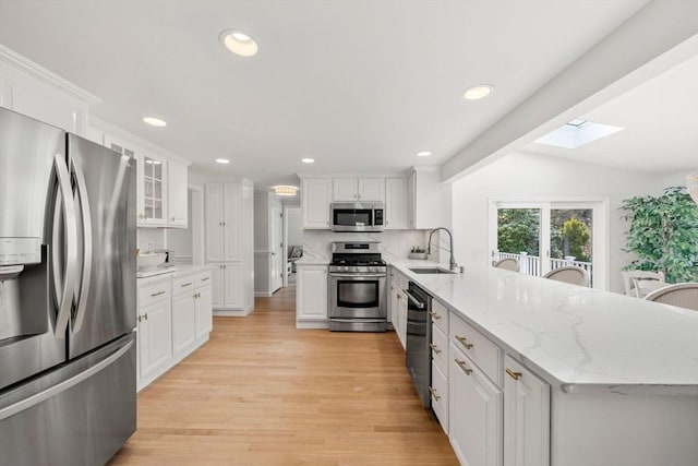 kitchen featuring a skylight, a sink, white cabinets, a peninsula, and stainless steel appliances