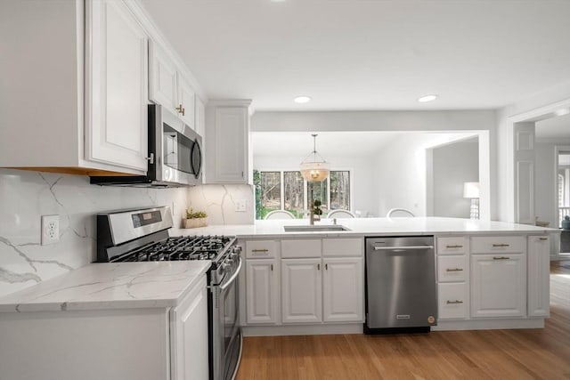 kitchen with a peninsula, white cabinetry, a sink, light wood-style flooring, and appliances with stainless steel finishes