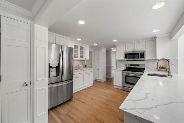 kitchen featuring crown molding, a sink, stainless steel appliances, white cabinetry, and backsplash