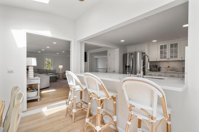 kitchen featuring decorative backsplash, visible vents, a sink, light wood finished floors, and glass insert cabinets