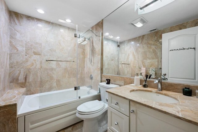 bathroom featuring vanity, toilet, tile walls,  shower combination, and visible vents