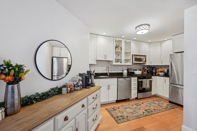 kitchen with a sink, stainless steel appliances, white cabinetry, backsplash, and glass insert cabinets