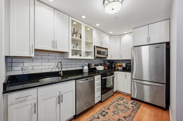 kitchen featuring glass insert cabinets, white cabinetry, tasteful backsplash, a sink, and stainless steel appliances