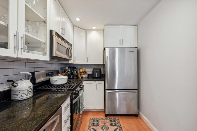 kitchen with glass insert cabinets, white cabinetry, tasteful backsplash, light wood-style flooring, and appliances with stainless steel finishes
