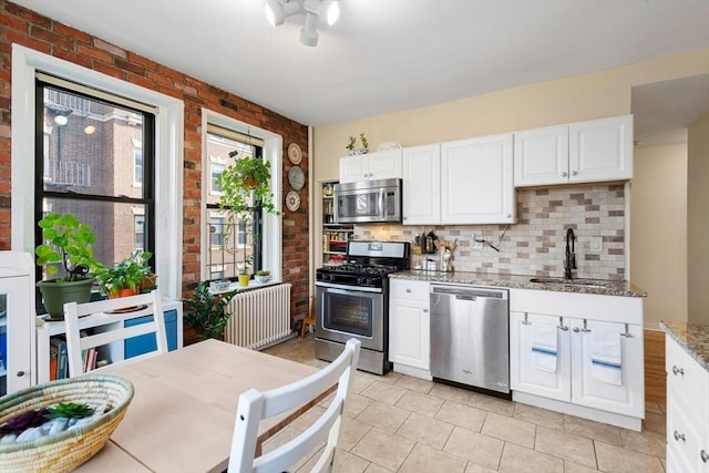 kitchen featuring appliances with stainless steel finishes, radiator heating unit, sink, white cabinets, and light stone countertops