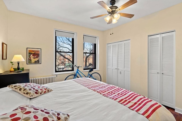 bedroom featuring two closets, dark wood-type flooring, radiator heating unit, and ceiling fan